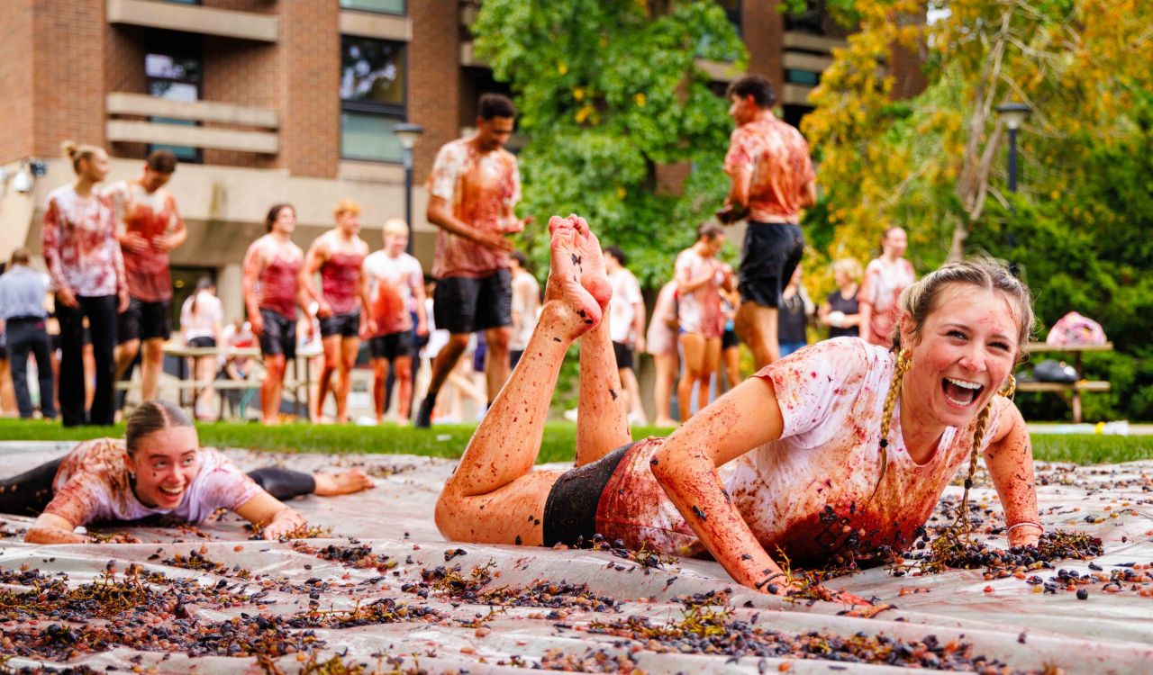 Students laughing while sliding through smashed grapes during the grape stomp event.