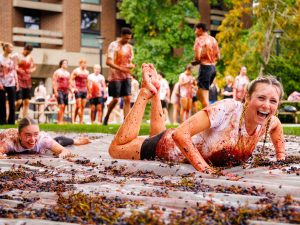 Students laughing while sliding through smashed grapes during the grape stomp event.