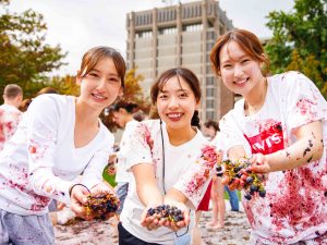 Three students holding bunches of grapes and smiling at the camera.