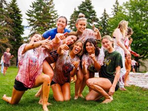 A group of seven students kneeling and posing together, laughing and pointing.