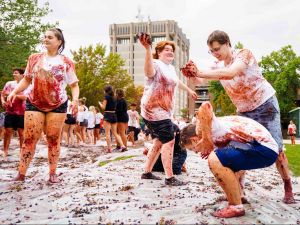 Students throwing grapes at each other on a juice-covered tarp while laughing.