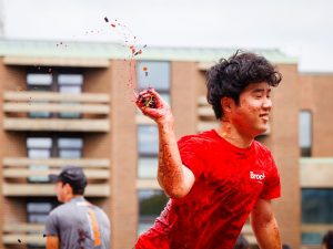 A participant smiling as he throws a handful of grapes, juice splattering in the air.