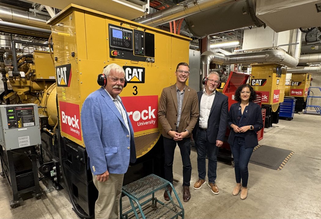 Four people stand in front of a generator