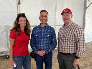 Three people pose for a photo in a tent at an agricultural fair.