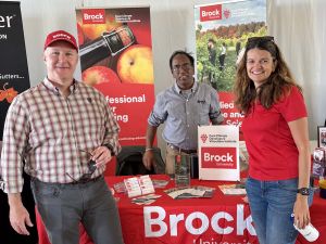 Three people stand at a Brock University booth at an agricultural fair.
