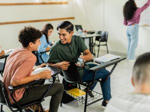 Two teenage boys laugh and sneak a look at a video on a cellphone while in class.