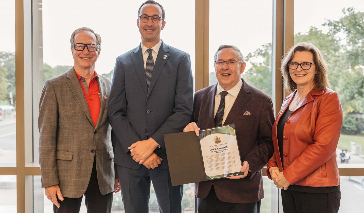 Four people stand together, one holding a ceremonial document.