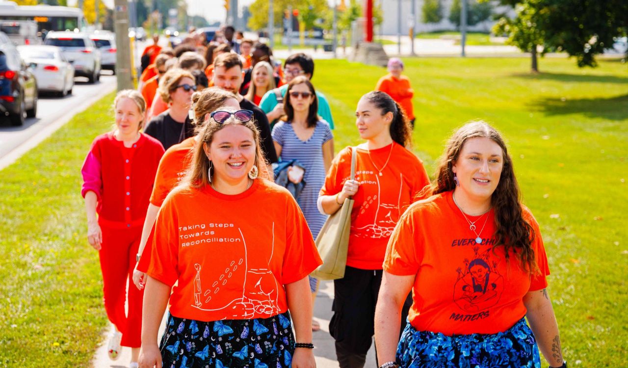 Members of the Brock University community in orange shirts walk together on Brock’s campus.