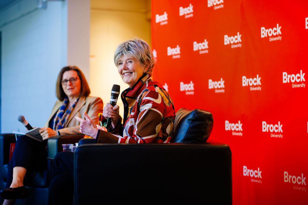 Two women sit at a table holding microphones.