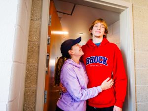 A mother hugs her teenage son in a doorway.