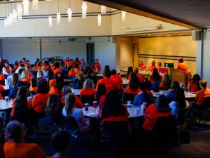 A large group of people sit at tables in an event space.