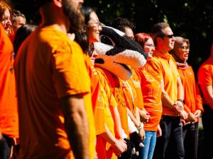 Group of people stand in a row wearing orange shirts.