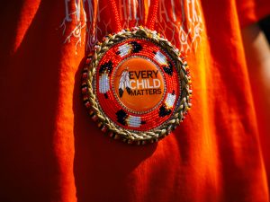 Beaded medallion reading Every Child Matters around a man’s neck.