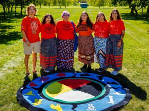 Group of five people stand in front of a medicine wheel mat.