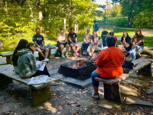 A group of students sit around a fire and talk.
