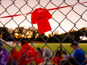 A small orange paper shirt with the name ‘Valerie’ hands on a chain-link fence at dusk.