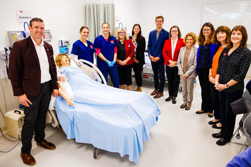 A group of people pose for a photo in a nursing lab.