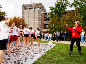 A woman takes a photo of university students who are posing at a grape stomp event.