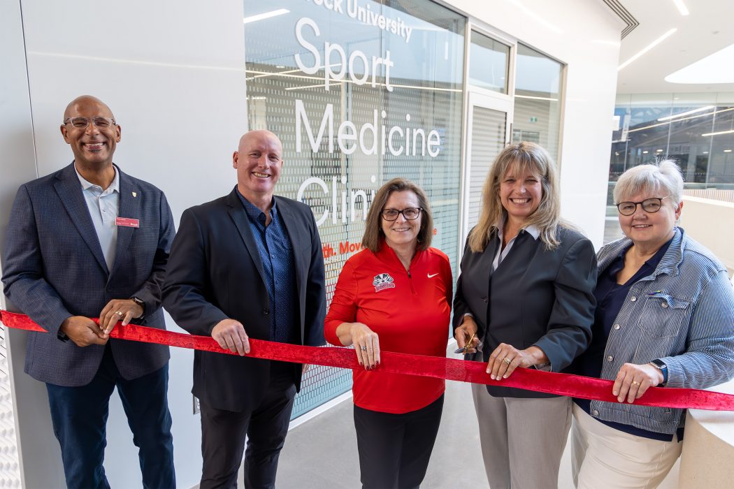 A group of five people hold a red ribbon at a ribbon-cutting ceremony.