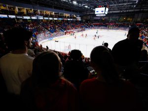 A packed arena full of people cheers during a hockey game.