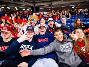 A large group of people cheer while sitting in seats in a packed arena.