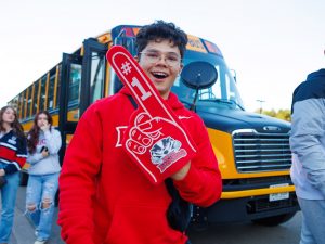 A man with an exaggerated red foam finger with the Brock Badgers logo on it stands in front of a yellow school bus.