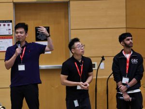 Three university students stand at the front of a lecture hall.