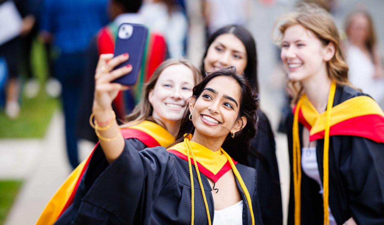 Four young women in graduation gowns pose for a selfie.