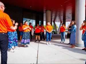 Participants wearing orange shirts stand outside listening to someone speak on Brock University’s campus.
