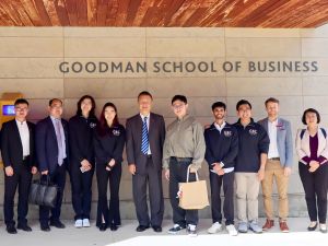 A large group of people pose under a Goodman School of Business sign.