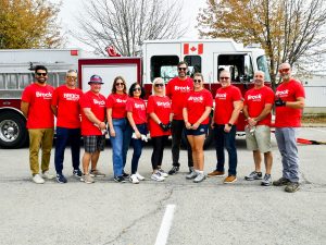 A group of people in red shirts pose for a photo in front of a fire truck.