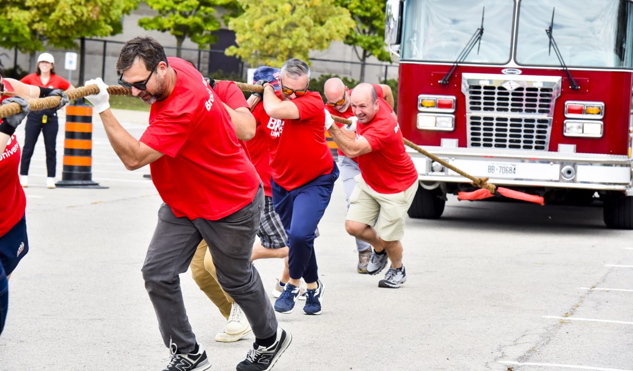 A group of people in red shirts pull a fire truck.