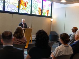 Man talks at a podium to a group of people.