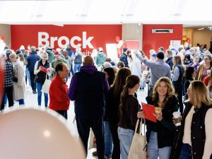 A large group of people walk through an information fair at Brock University.