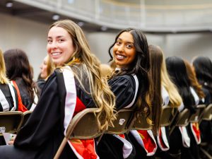 Two graduates turn and smile during the convocation ceremony.