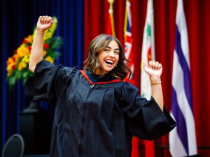 A joyful graduate raises her arms in celebration on stage.