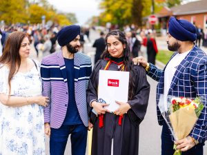 A graduate poses with family after the ceremony, holding flowers and her degree.