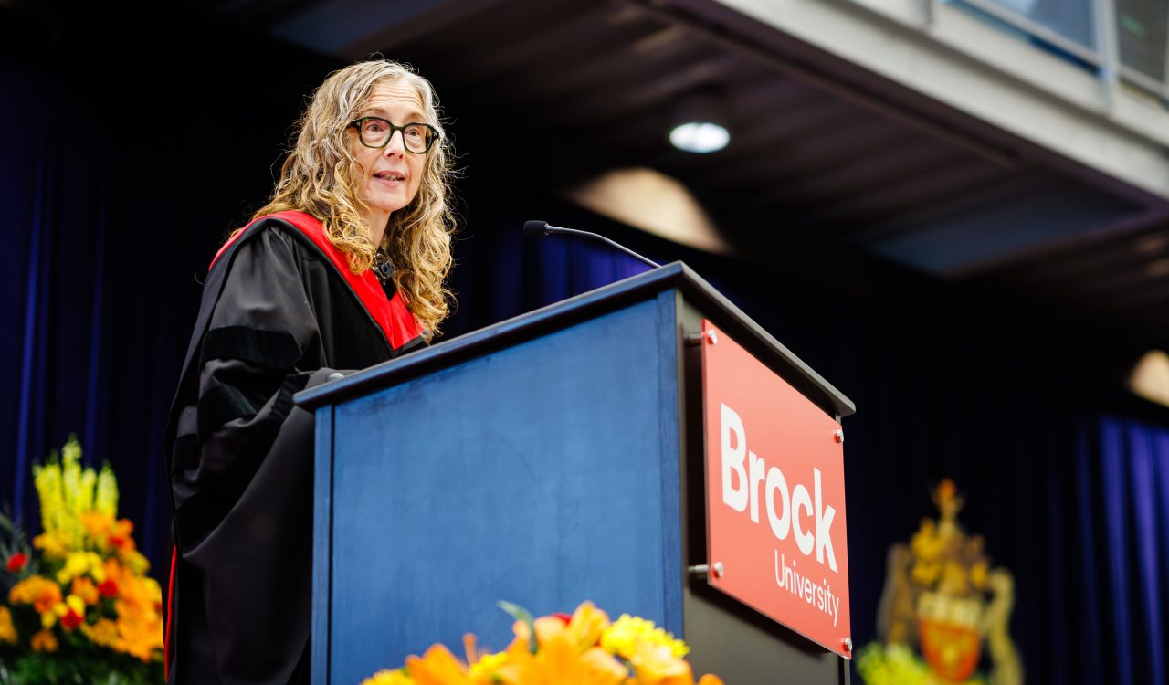 A woman speaks at a podium during a university graduation ceremony.