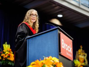 A woman speaks at a podium during a university graduation ceremony.