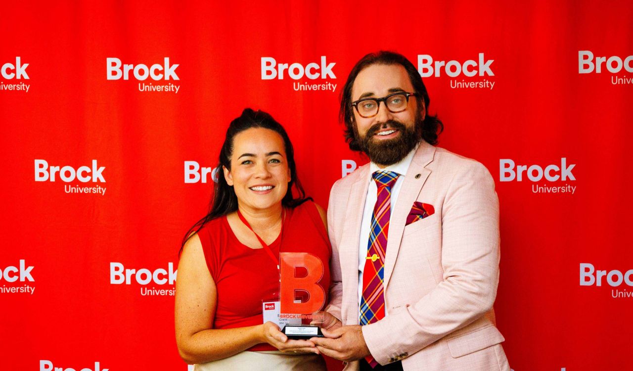Two people pose with an award in front of a red backdrop.