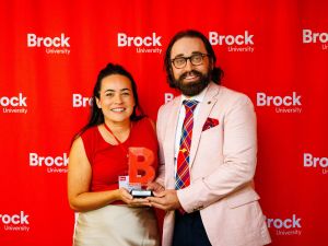 Two people pose with an award in front of a red backdrop.