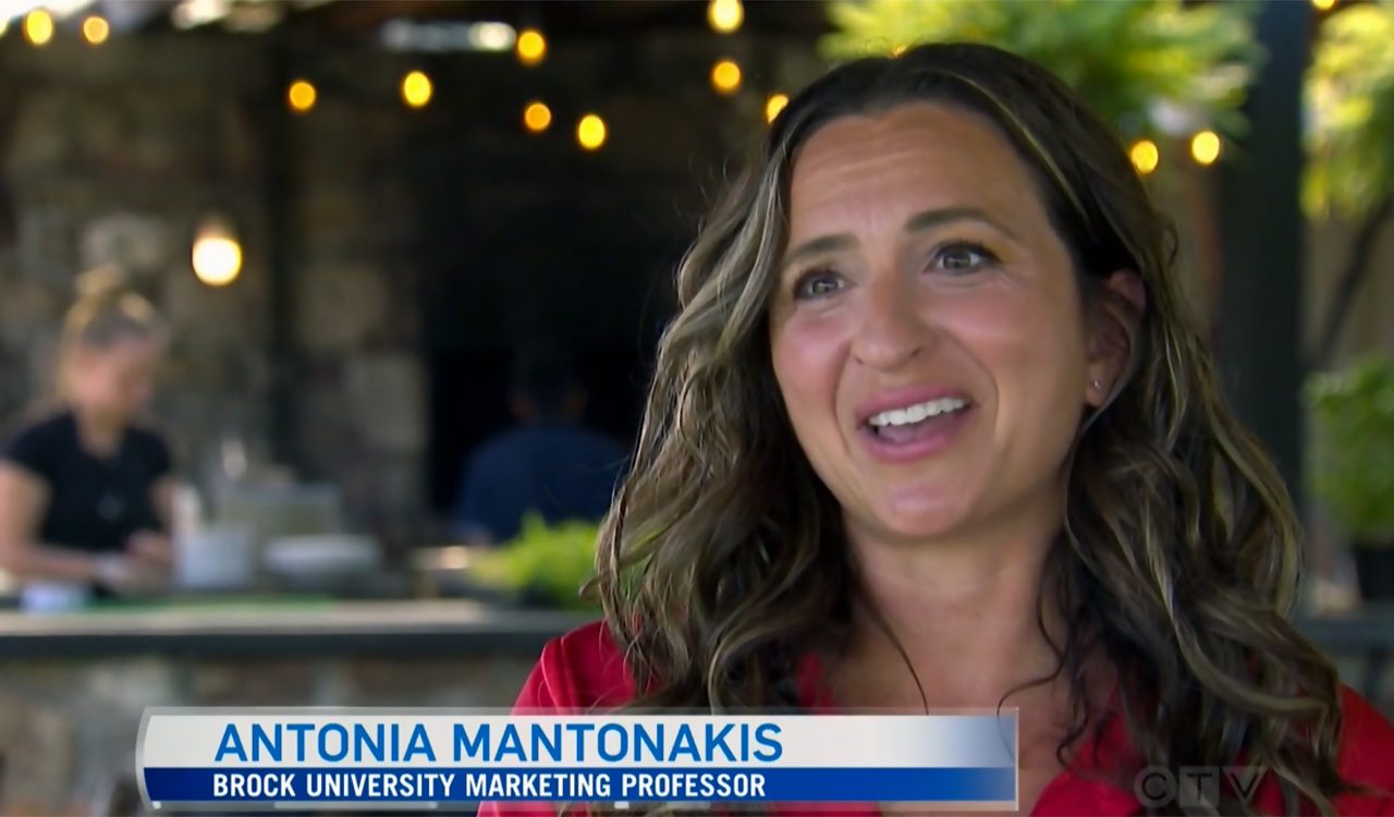 Woman does a television interview at a table with lights in the background.