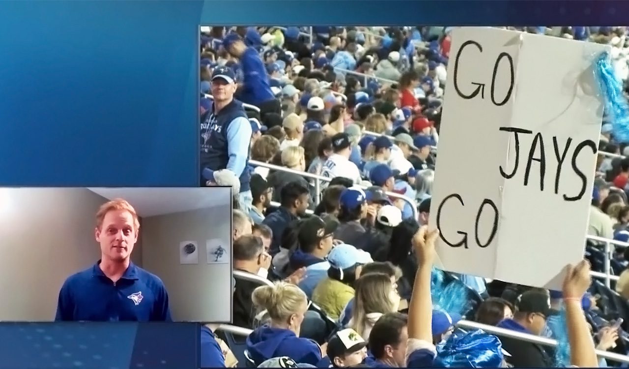 Man wears blue jays shirt and talks about a video showing a crowd of sports fans.