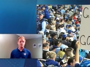 Man wears blue jays shirt and talks about a video showing a crowd of sports fans.