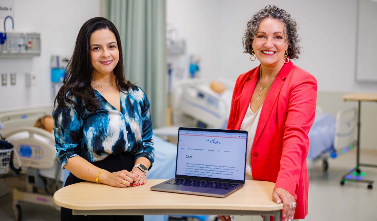 Two women stand beside a table holding a laptop.