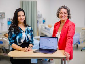 Two women stand beside a table holding a laptop.