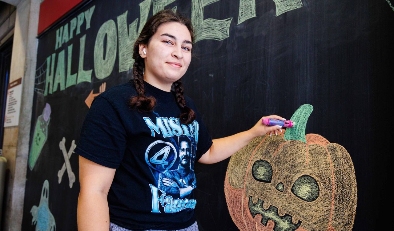 A young woman smiles while drawing on a chalkboard.