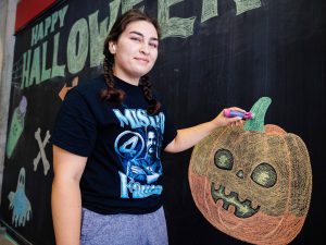 A young woman smiles while drawing on a chalkboard.