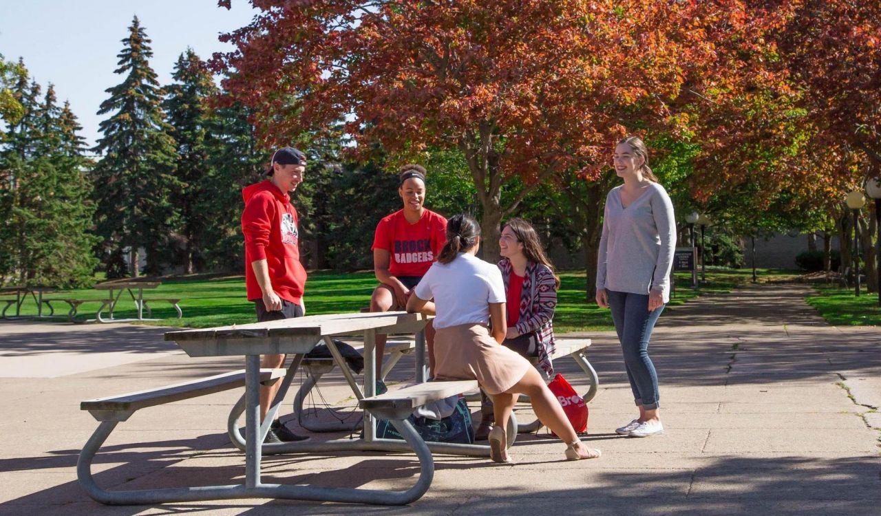 A group of university students sits at a picnic table in a courtyard.