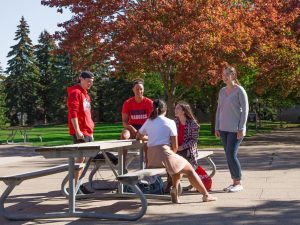 A group of university students sits at a picnic table in a courtyard.
